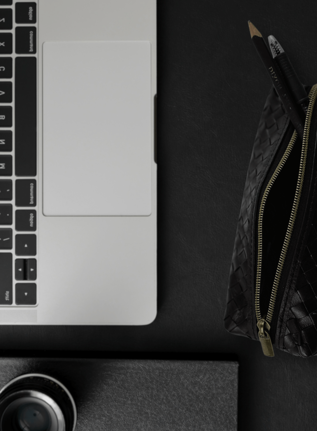 Black woven pencil case with laptop and supplies flat lay.