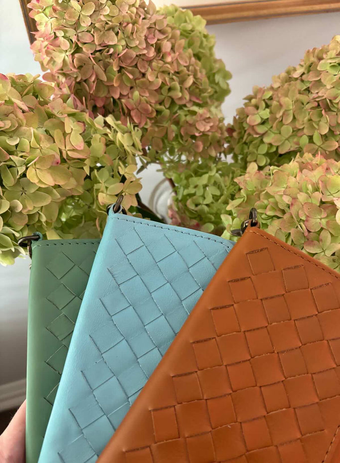 model sitting and leaning on a box holding the woven wristlets in sky blue and sage green.