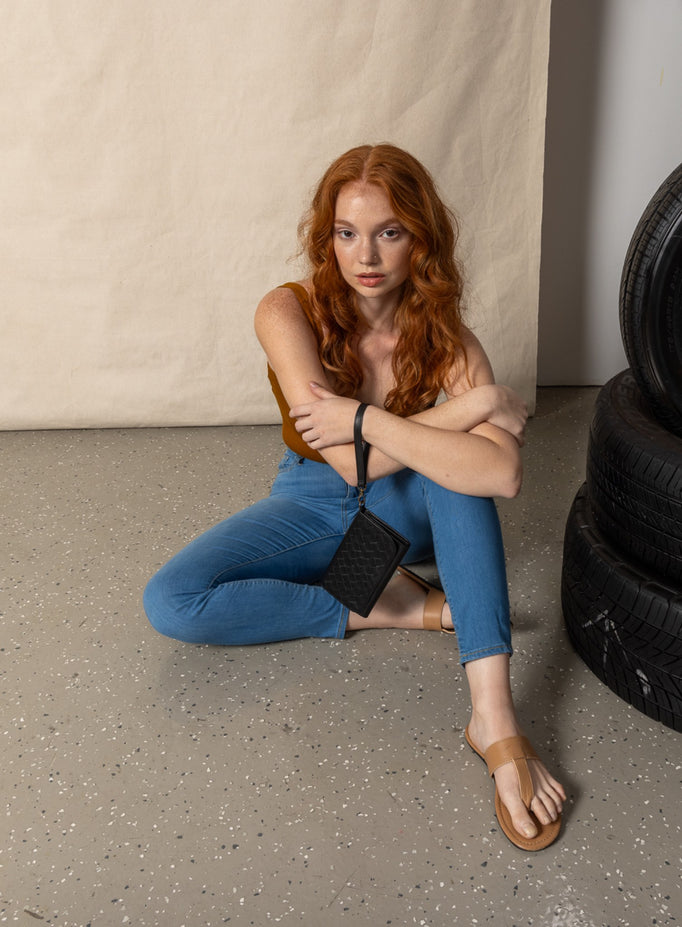 model sitting and leaning on a box holding the woven wristlets in sky blue and sage green.